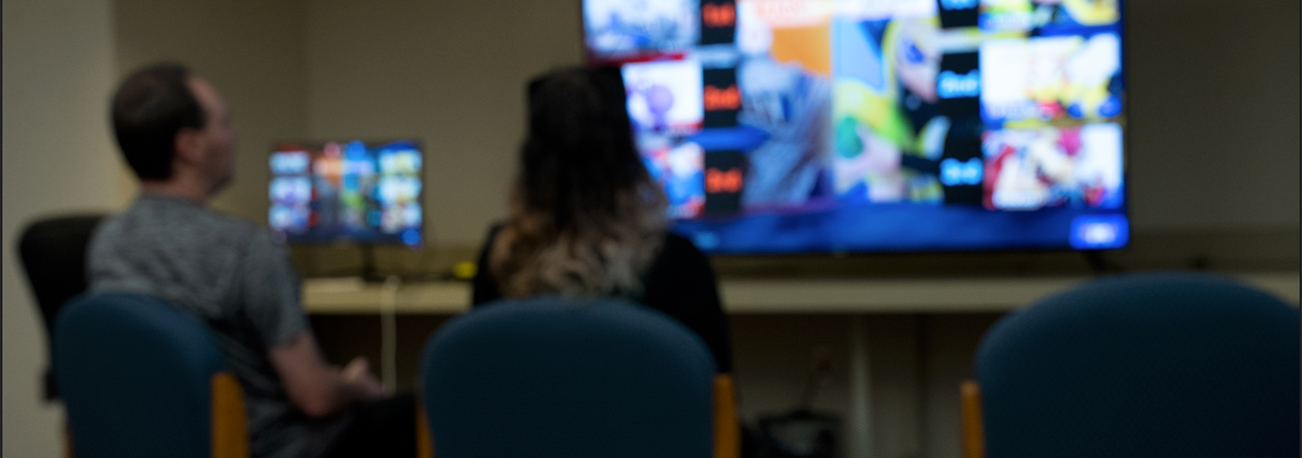 Two people face a big screen television.
