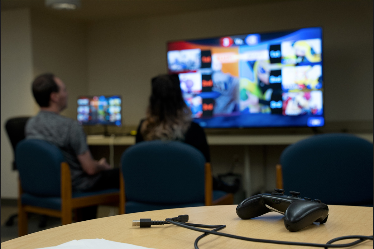 Two people face a big screen television.