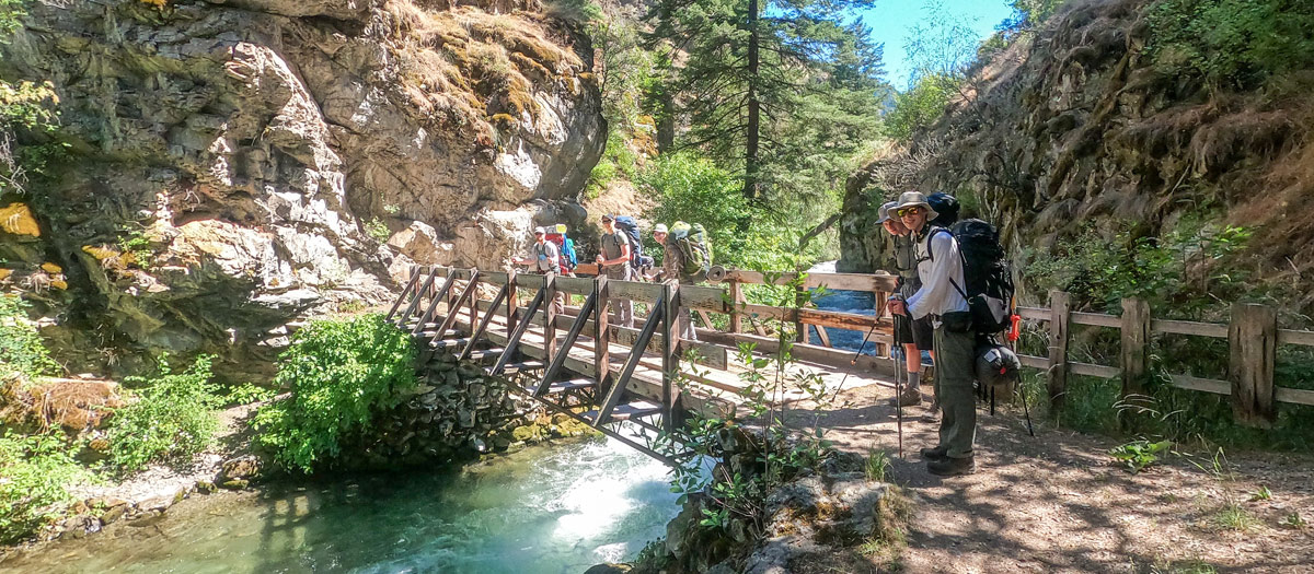 Hikers use a bridge to cross a creek.