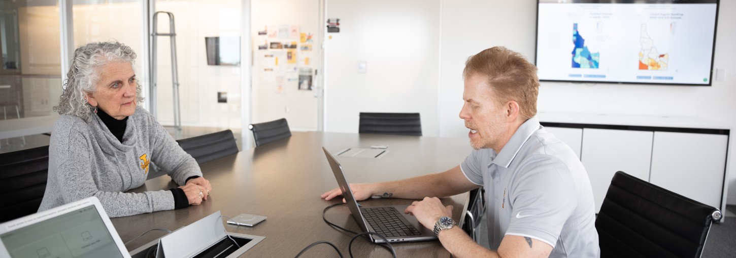 Researchers talk at a meeting table, while a screen shows color-coded maps of Idaho.