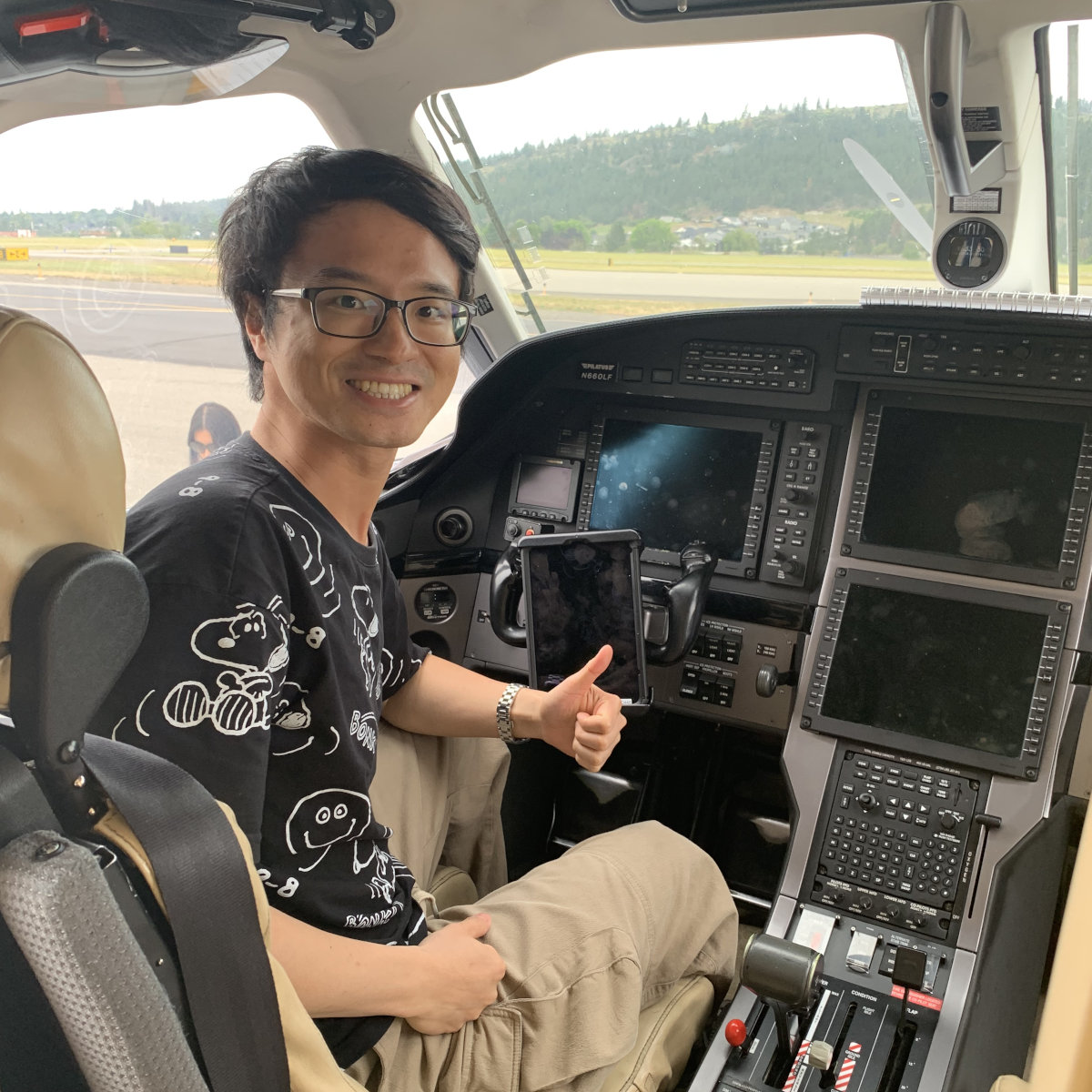 Liang Liang smiles while seated at the front of a helicopter with controls all around.