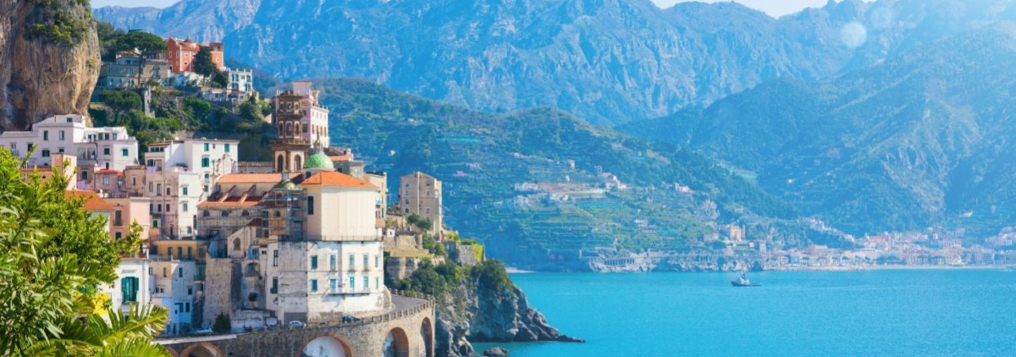 A view of the Amalfi Coast with a village and rolling mountains surrounding the water.
