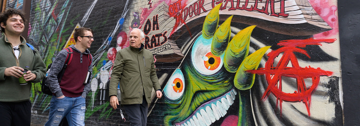 Students and a professor walk by a wall with a mural on it.