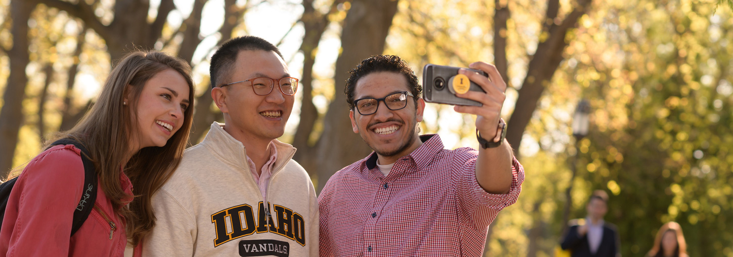 A student takes a selfie with two friends on the Administration Lawn.