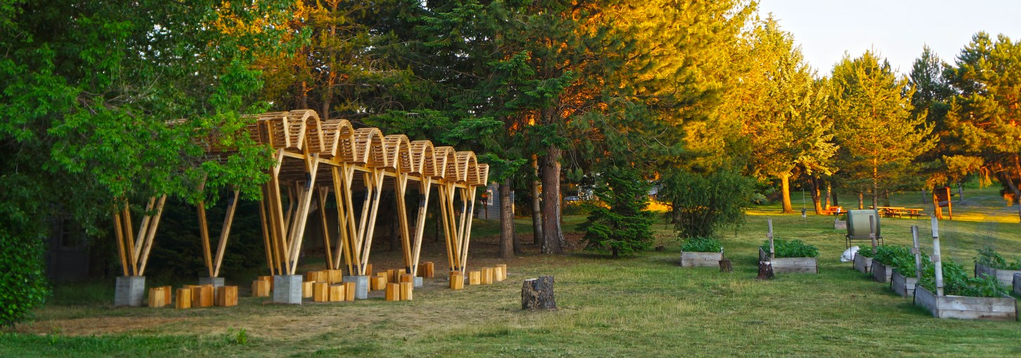 A rolling roof and V-shaped framed outdoor classroom sits before trees.