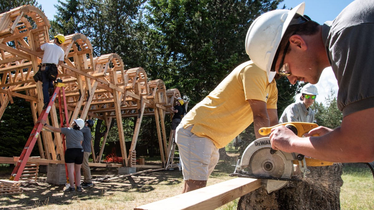 A stude3nt cuts lengths of framing while others place them into the roof structure.