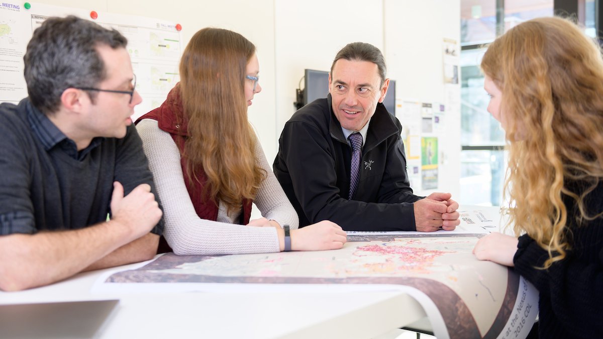 INFEWS researchers stand around a table with a map on it, smiling and talking.
