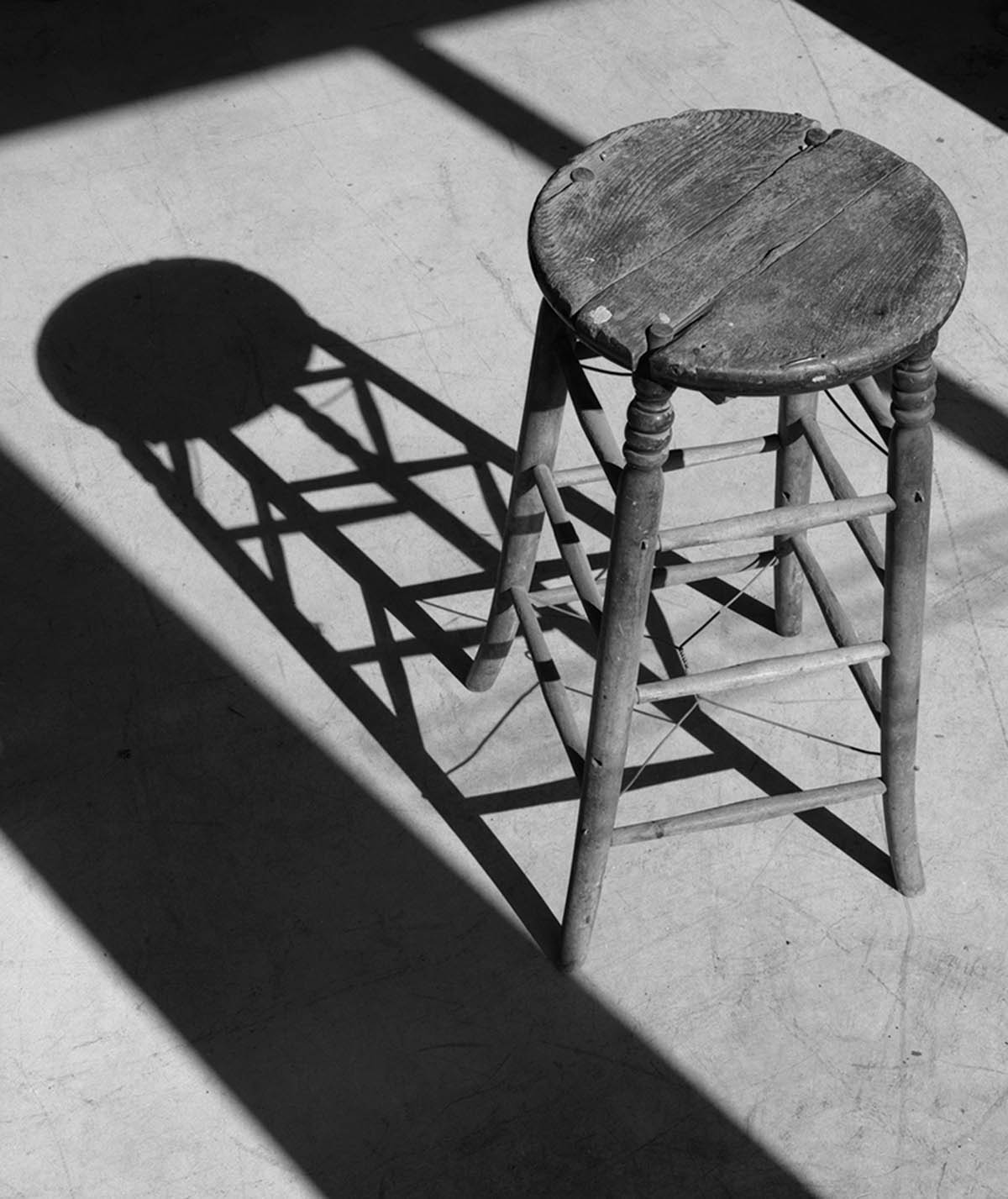 Black and white photograph of an old wooden stool and the shadow it casts on the floor.