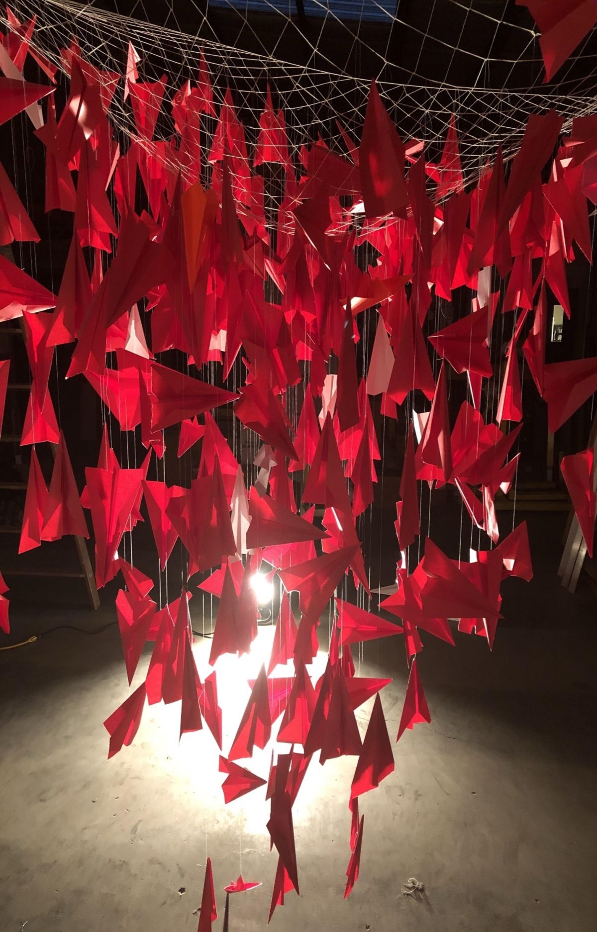 Installation of a large number of red paper airplanes suspended from a ceiling. 