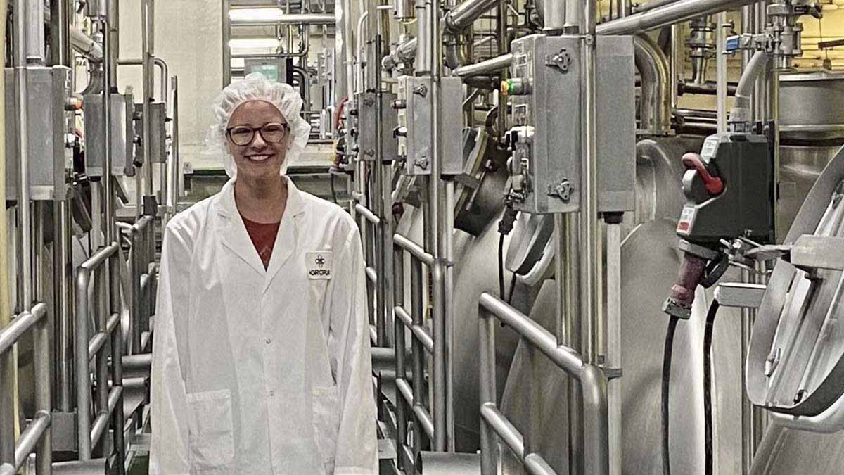 A woman stands between vats of milk at a cheese processing facility.