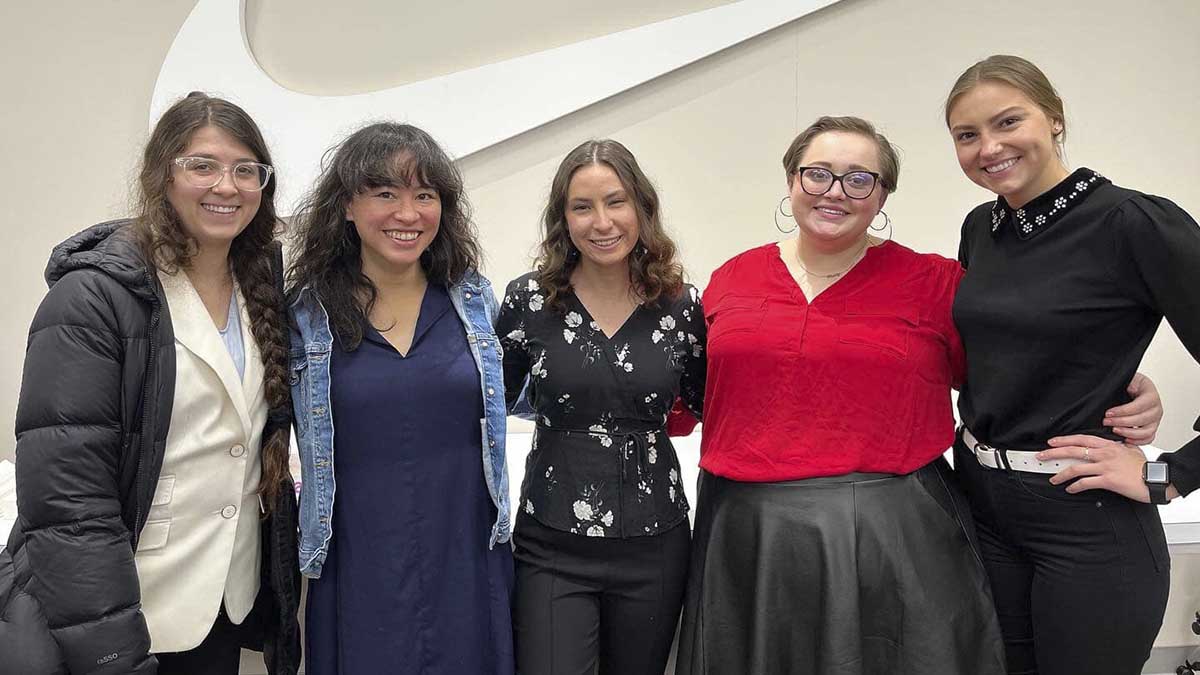 Five women pose in front of the Nike swoosh logo.