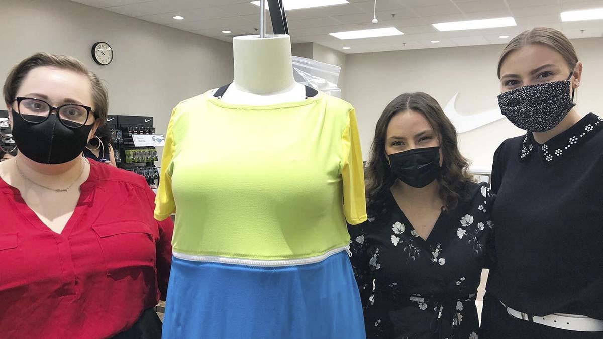 Three women stand next to dress form wearing swimsuit coverup.
