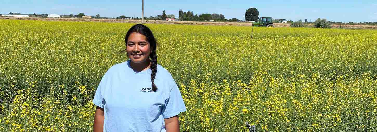 A woman stands in a field of canola plants.