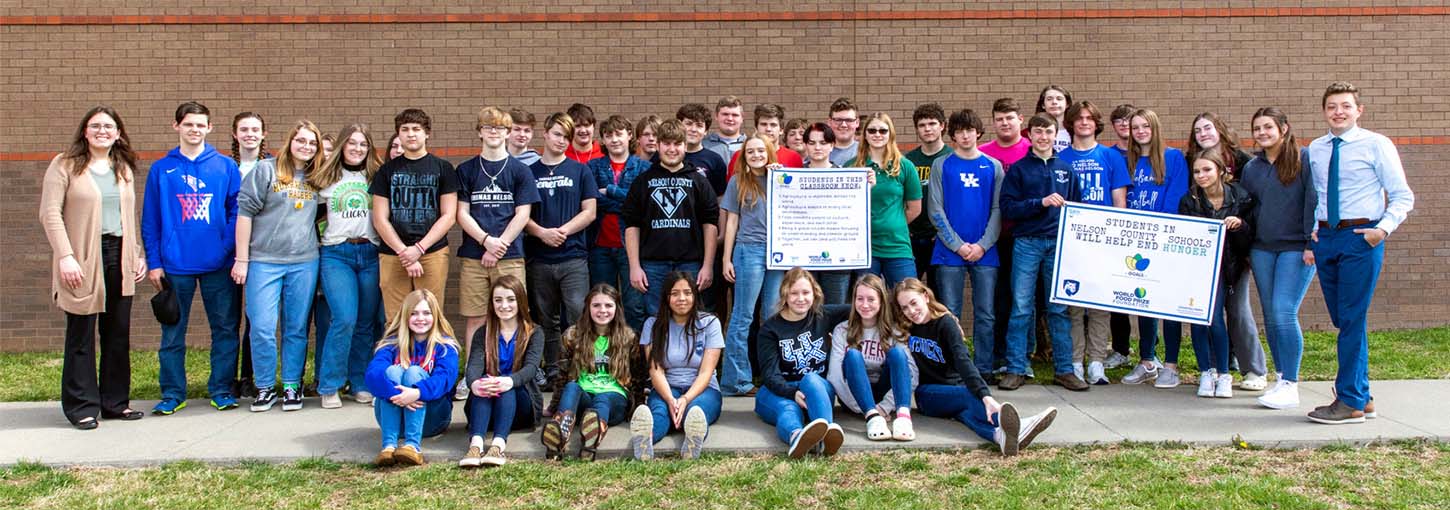 Group of students and teachers stand outside of a high school building.