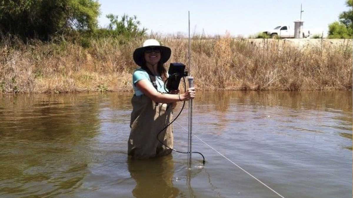 A woman takes stands in a river to take water measurements.