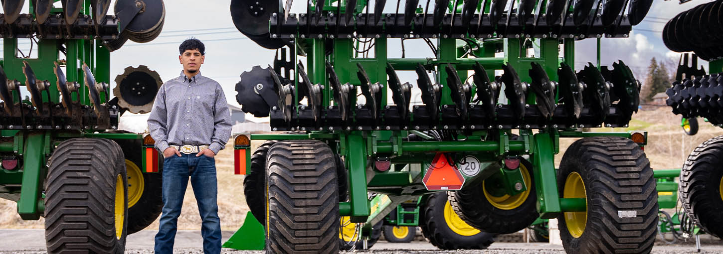 A man stands in front of a row of John Deere combines.
