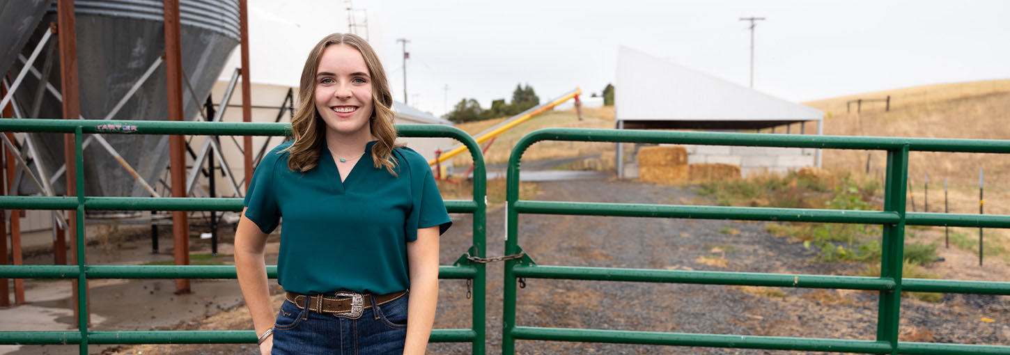 A woman poses outside in front of a green fence.