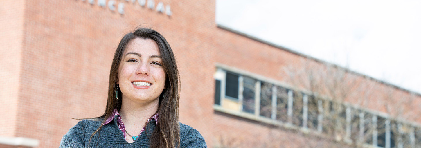 A woman poses outside of a brick building on the University of Idaho campus.