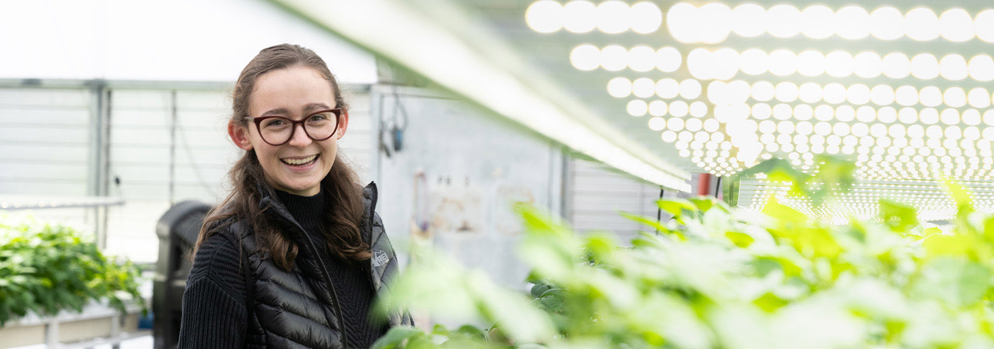 A woman stands next to potato plantlets in a greenhouse.