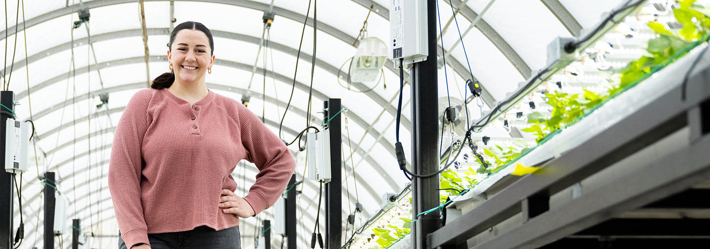 A woman stands next to potato plantlets in a greenhouse.