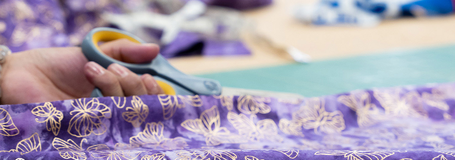 A close up shot of a person using scissors to cut purple fabric.
