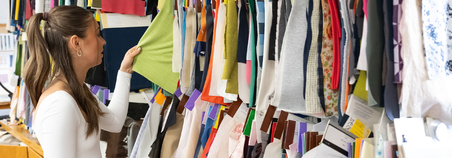 A woman browses through hangers of fabric.