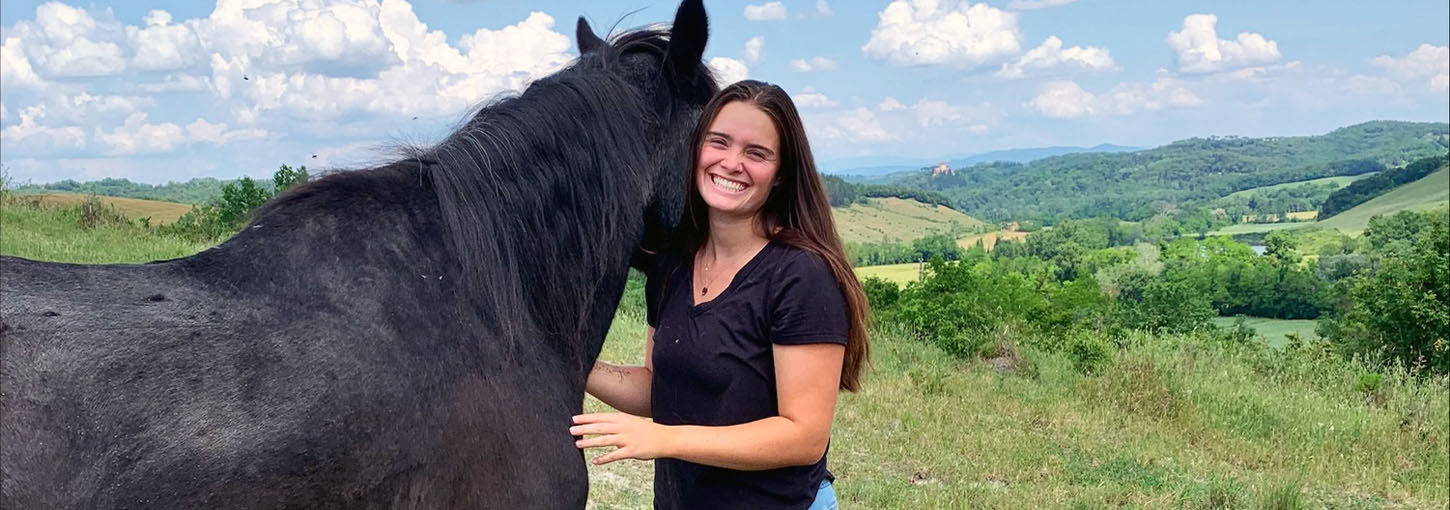 A woman stands next to a horse in the Italian countryside.