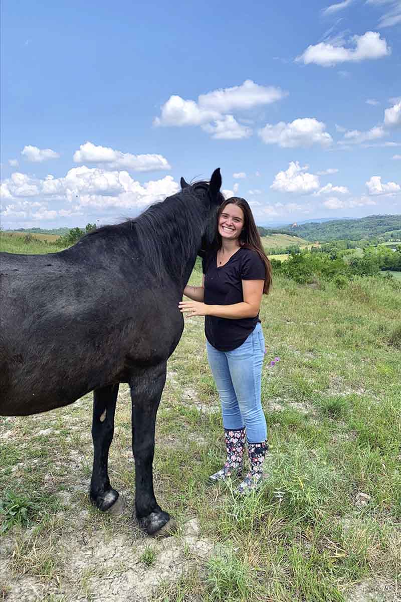 A woman stands next to a horse in a pasture.