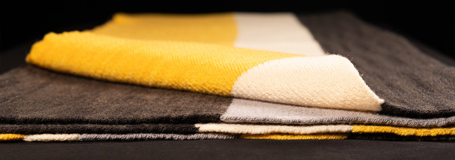 A folded black, grey, gold and white striped wool blanket.