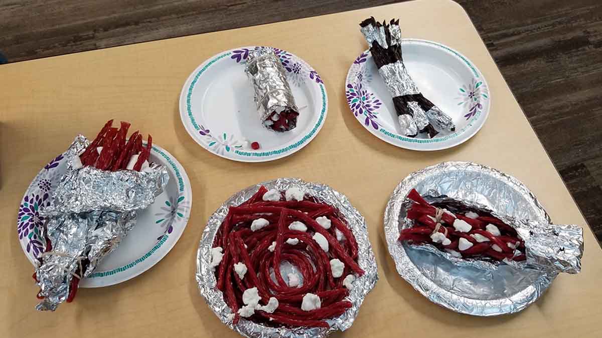 Plates full of Twizzlers and marshmallows connected by aluminum foil and rubber bands.