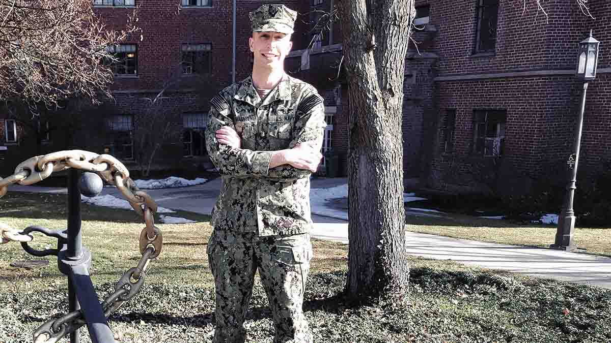 Man in camouflage fatigues stands near boat anchor.
