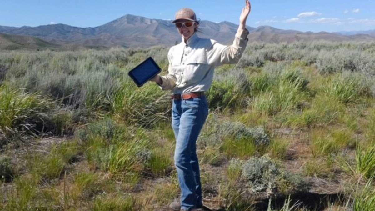 A student stands amongst sagebrush with a tablet.