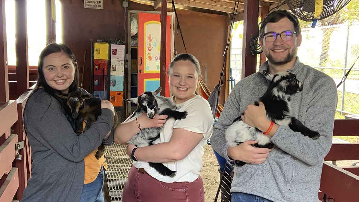 Two women and one man holding baby goats.
