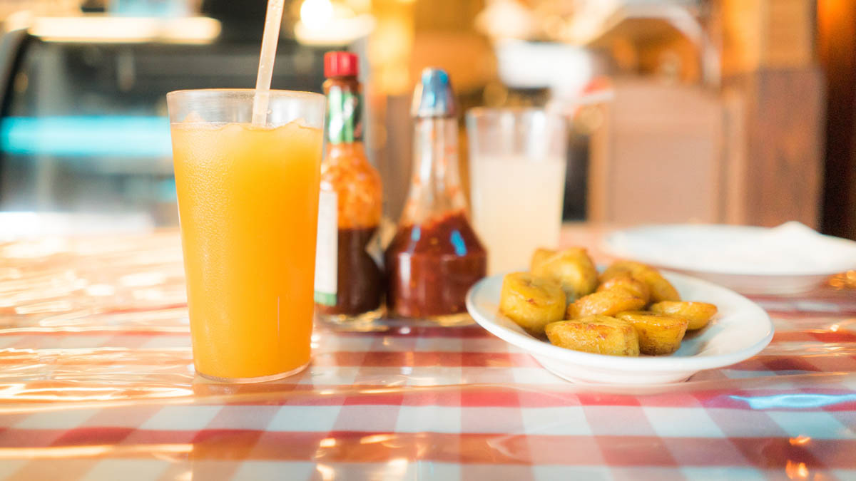 A glass of orange juice, sauce and scallops on a red and white checkered table cloth.