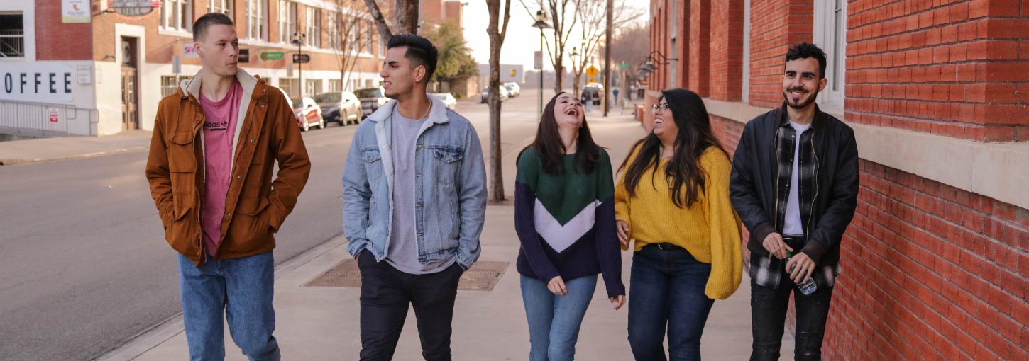 Five young adults walk down an urban street. 