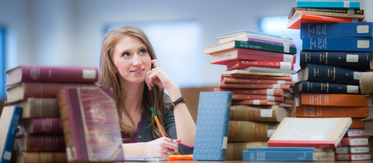 A student surrounded by books in the library.