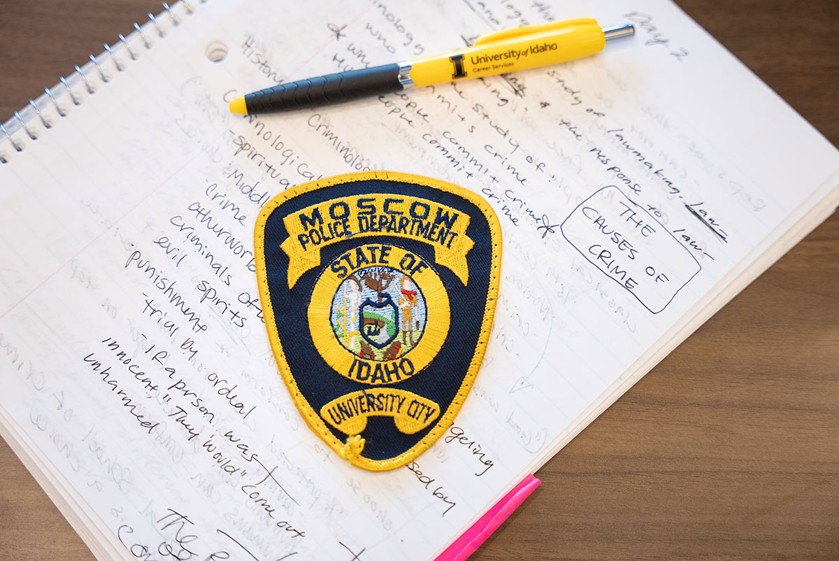 A police patch on a notebook page with hand-written notes.