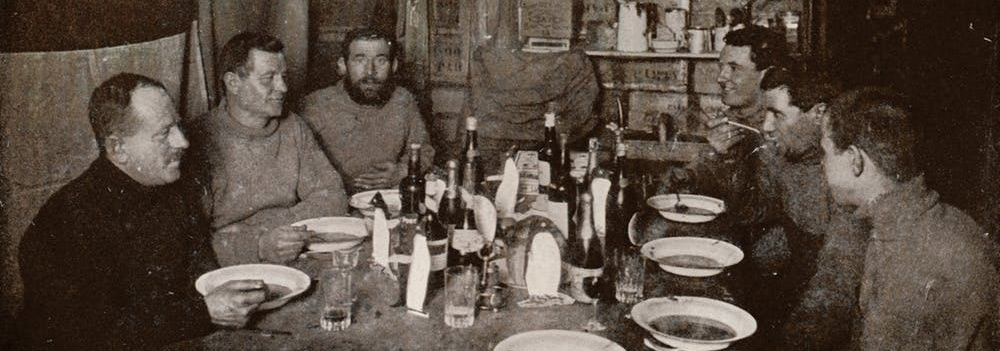 Six members of Robert Falcon Scott’s Terra Nova Expedition gather around a table for a meal in 1912.