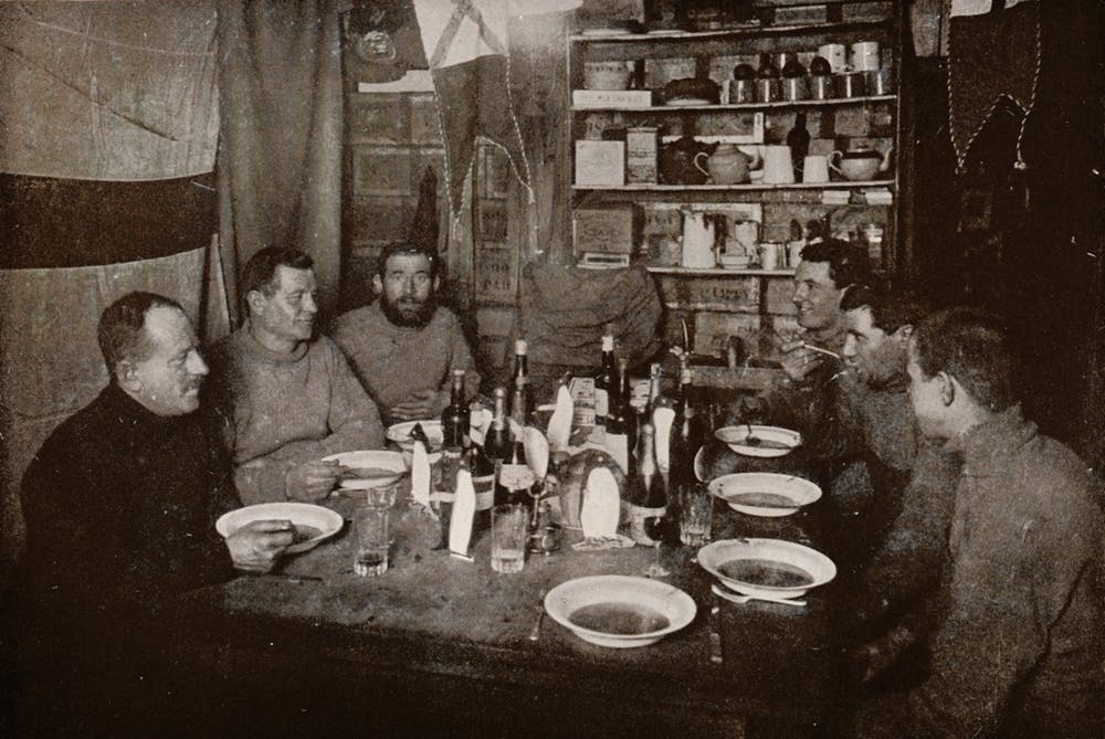Six members of Robert Falcon Scott’s Terra Nova Expedition gather around a table for a meal in 1912.