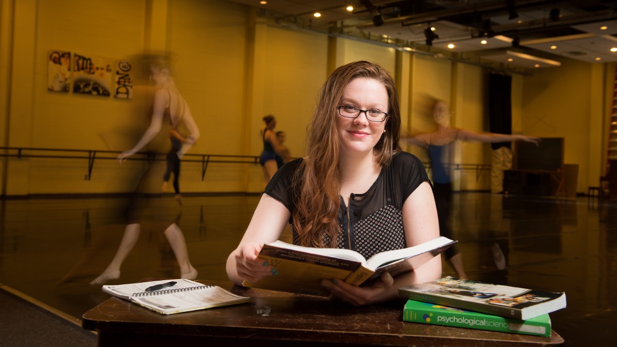 Student studies while dancers move around in the background.