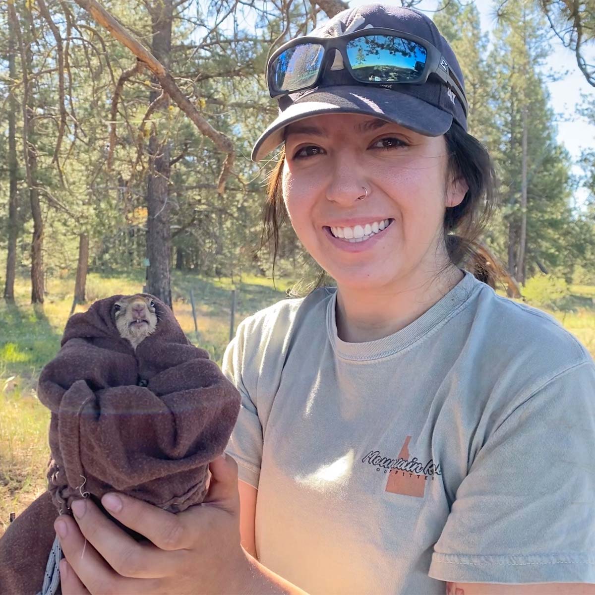 Smiling researcher holds ground squirrel wrapped in a towel.
