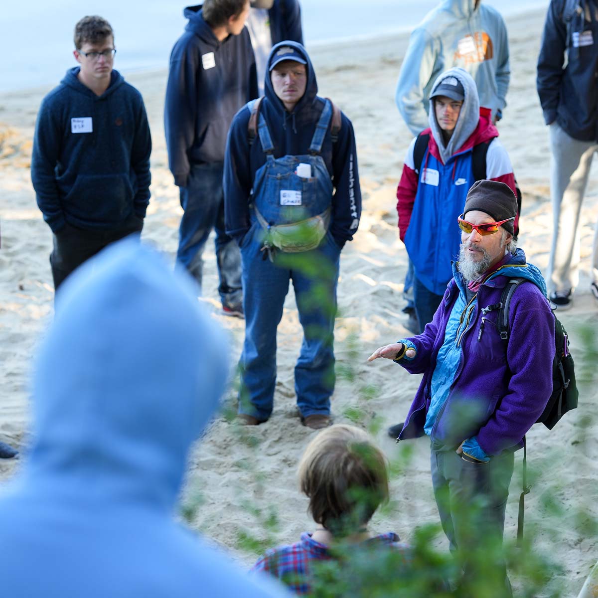A man talks to students on beach.