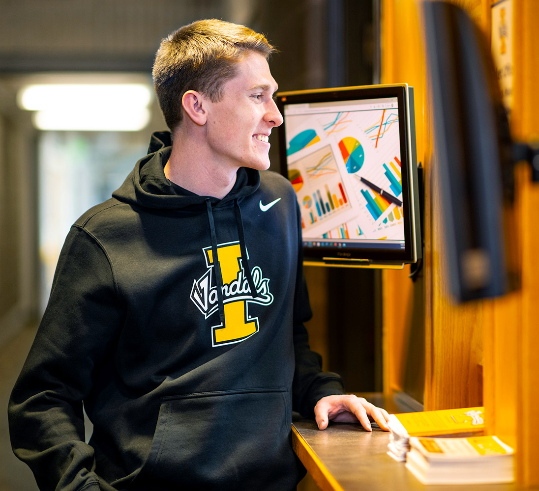 Young man wearing a black, Vandals sweatshirt smiles at ticket window attendant.
