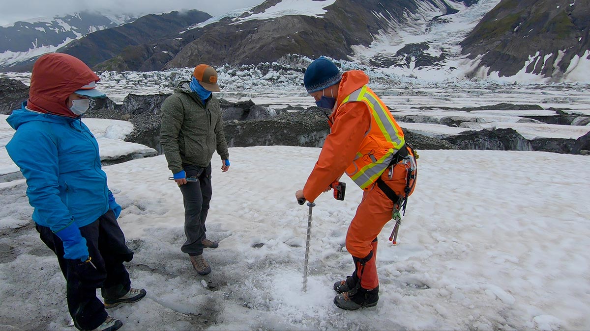 Three people work with an auger to drill into Turner Glacier