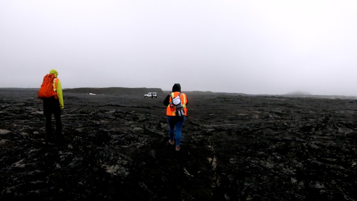 Researcher walks across black Icelandic lava flow.