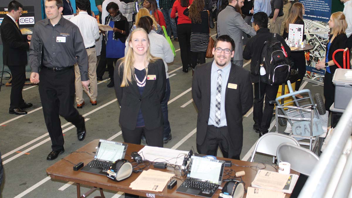 An intern helps his supervisor at the Career Fair check-in station