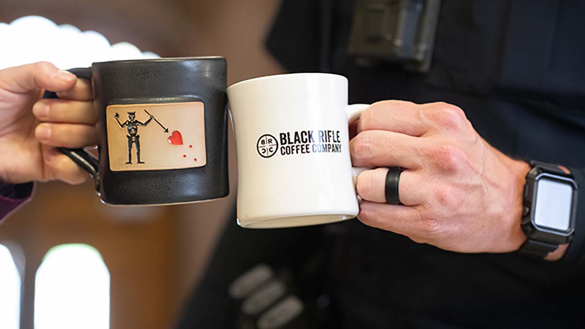 Two veterans hold coffee mugs with logos from the Black Rifle Coffee Company.