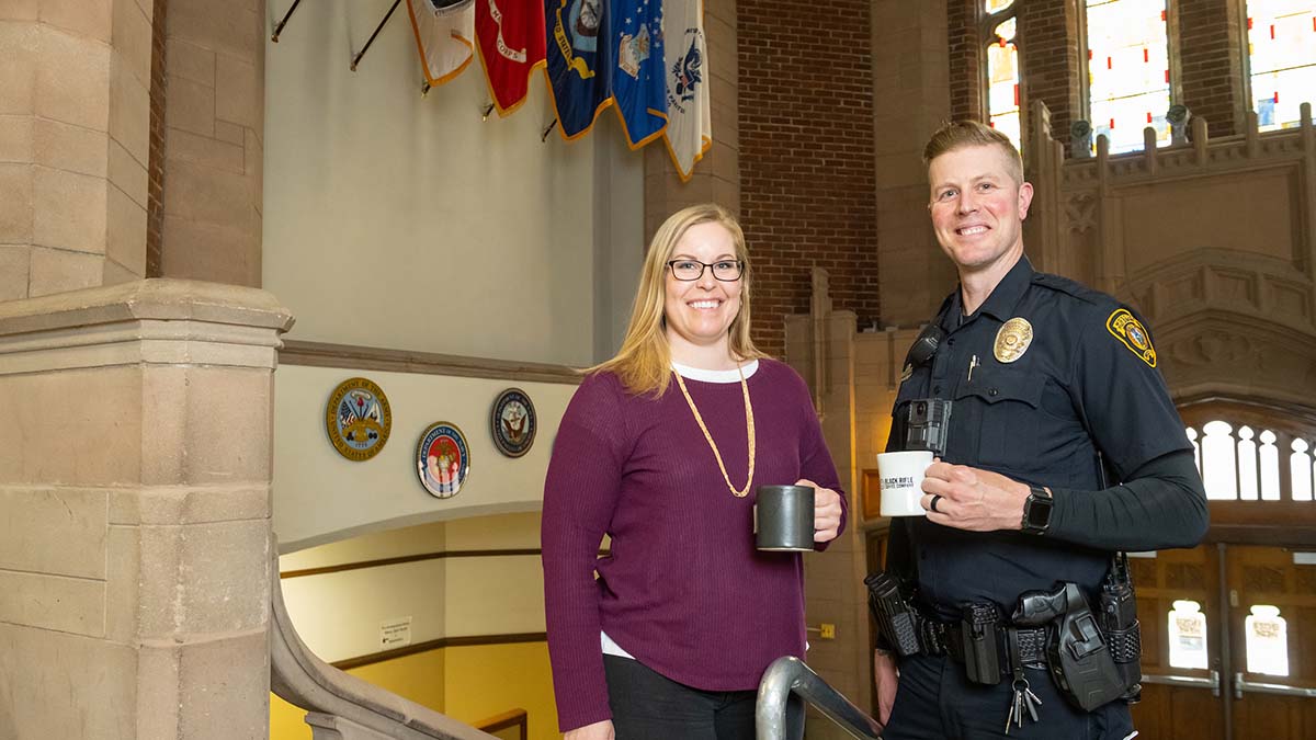 Alumni and Operation Education scholarship recipients Jennifer Tengono and Jason House hold coffee mugs in the lobby of the Memorial Gym