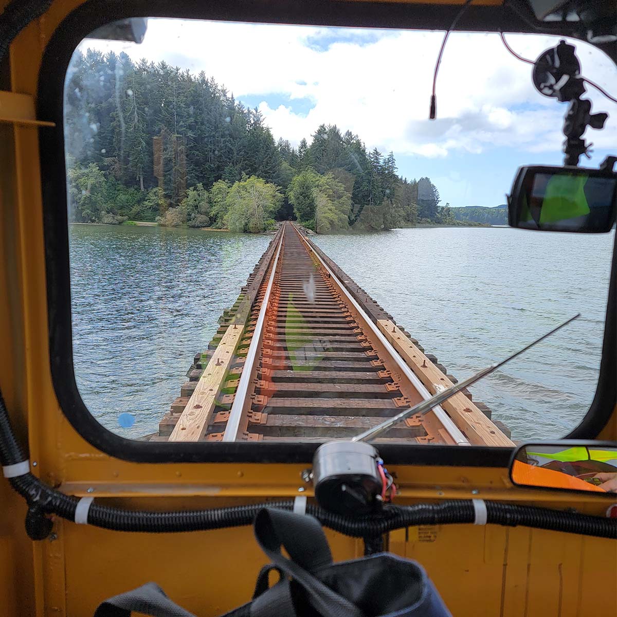 Looking out of the front of Grigg’s railroad car on a bridge over a body of water, into a tunnel heading through densely forested area.