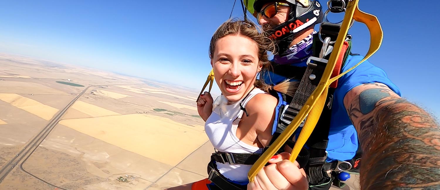 University of Idaho student Claire Qualls smiles at camera mid air self portrait during tandem skydive parachute over central Washington